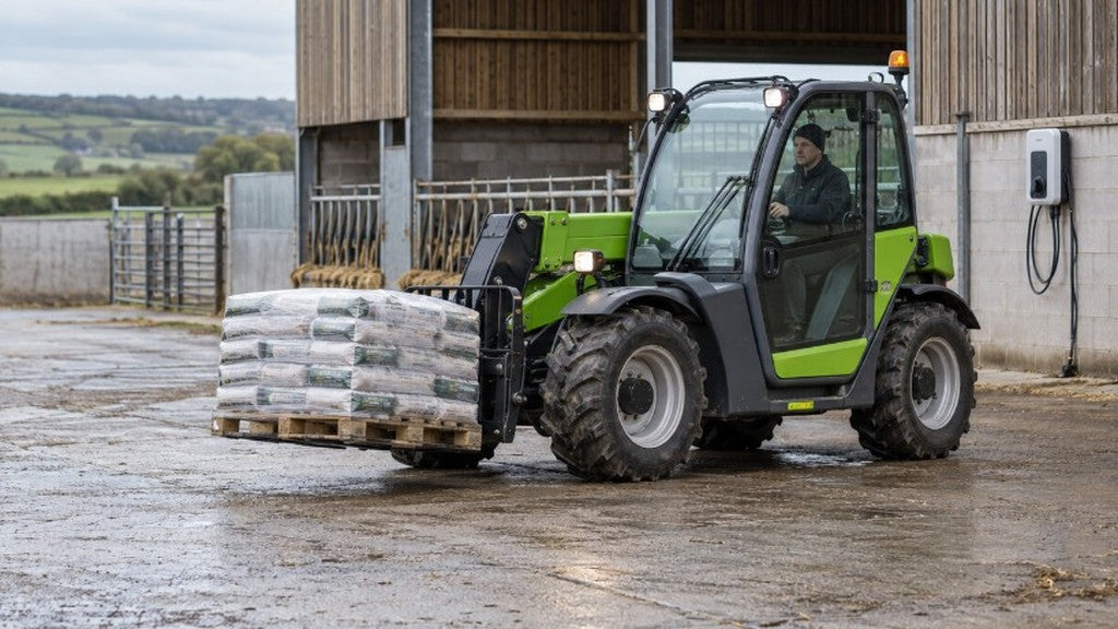 Electric agricultural telehandler handling a pallet safely in a British farmyard near its charging point.